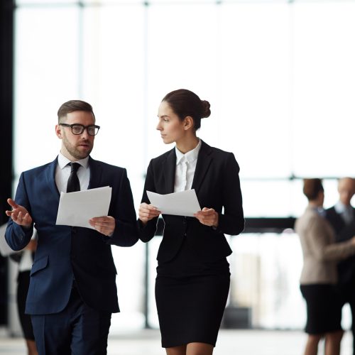 Two,Young,Confident,Politicians,With,Papers,Discussing,Details,Of,Their Two young confident politicians with papers discussing details of their joint report or presentation while walking to conference hall