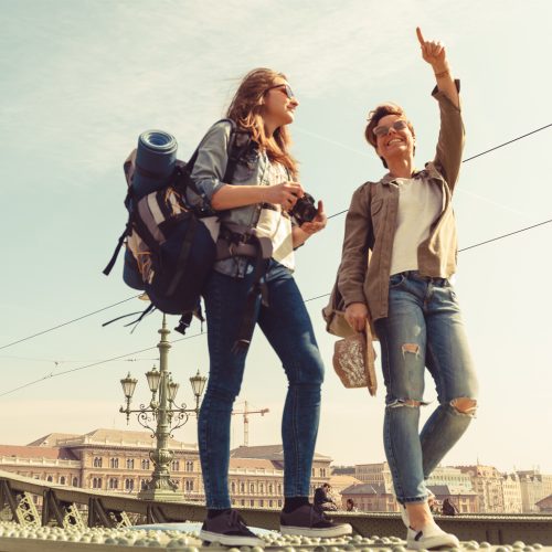 Two young girlfriends traveling, walking on a bridge, enjoying the sunny day and the sightseeing of the city